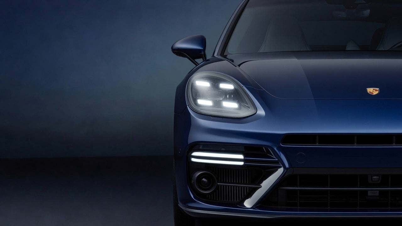 Close-up of a blue Porsche car's front headlight and grille on a dark background